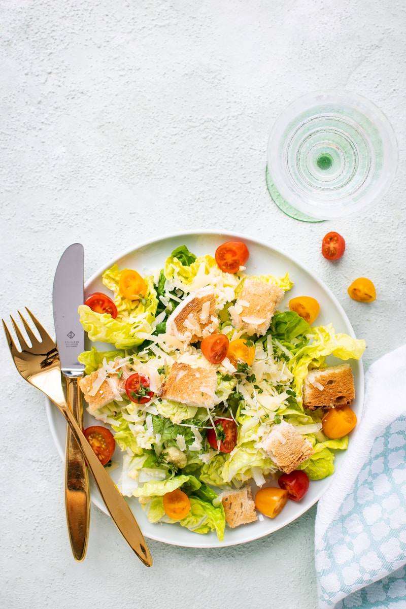 Fresh garden salad with romaine lettuce, cherry tomatoes, croutons, and grated cheese, served on a white plate with golden cutlery.